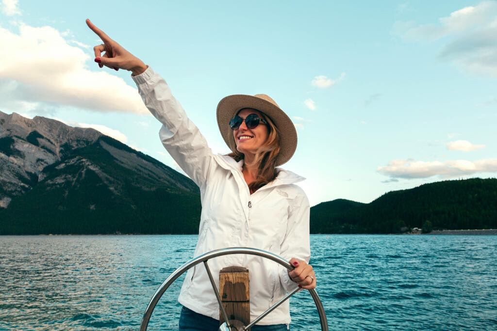 Femme souriante sur un bateau au bord d'un lac entouré de montagnes
